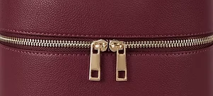 Close detail of the gold twin-pull zip running across the grained burgundy leather.