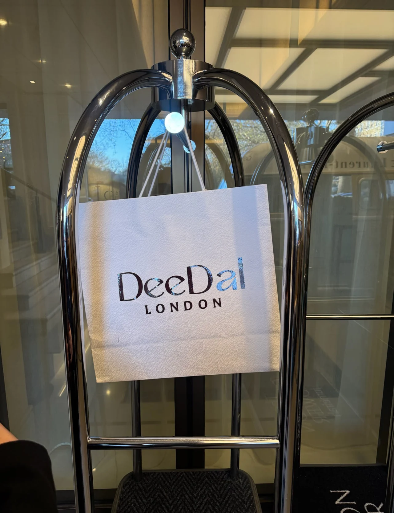 A DeeDal London bag on a luggage stand at a Knightsbridge hotel entrance.