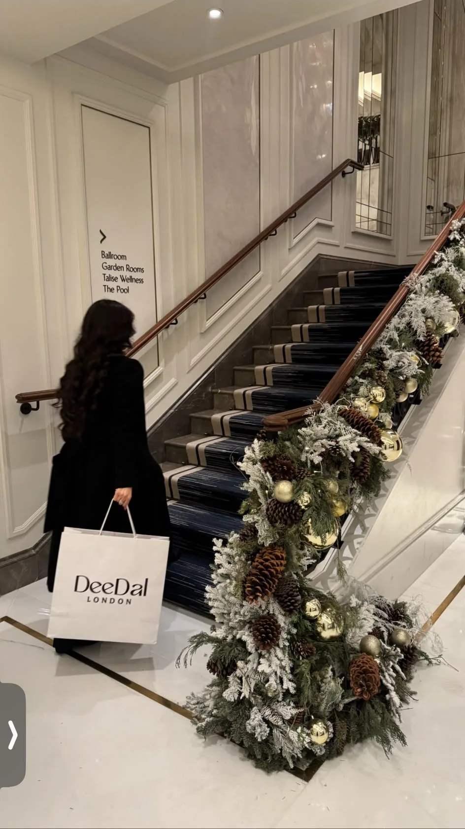 A woman carrying a DeeDal London bag up a hotel staircase dressed with a winter garland.