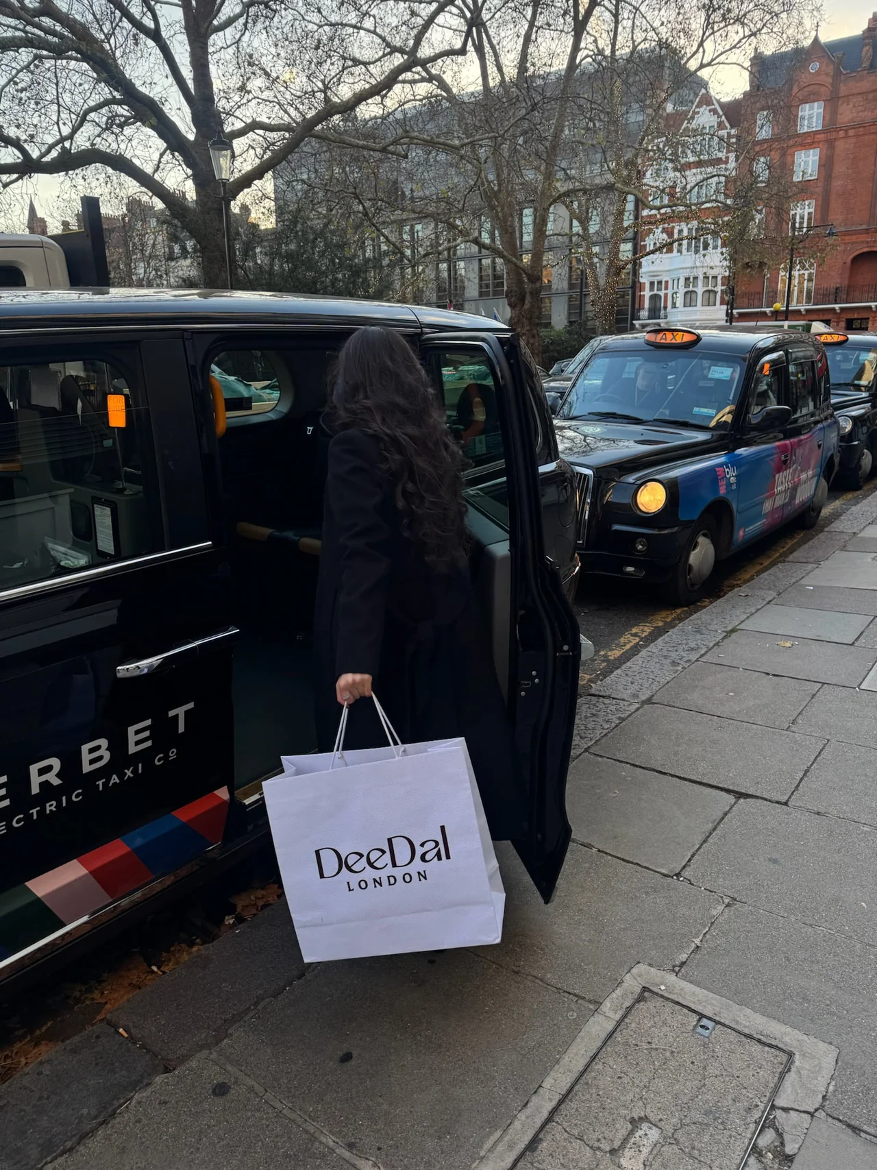 A woman stepping into a black cab with a DeeDal London bag.